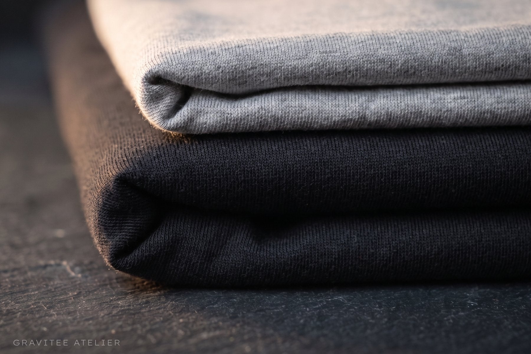 Two folded cotton t-shirts stacked, a lighter-weight jersey resting on a heavier one